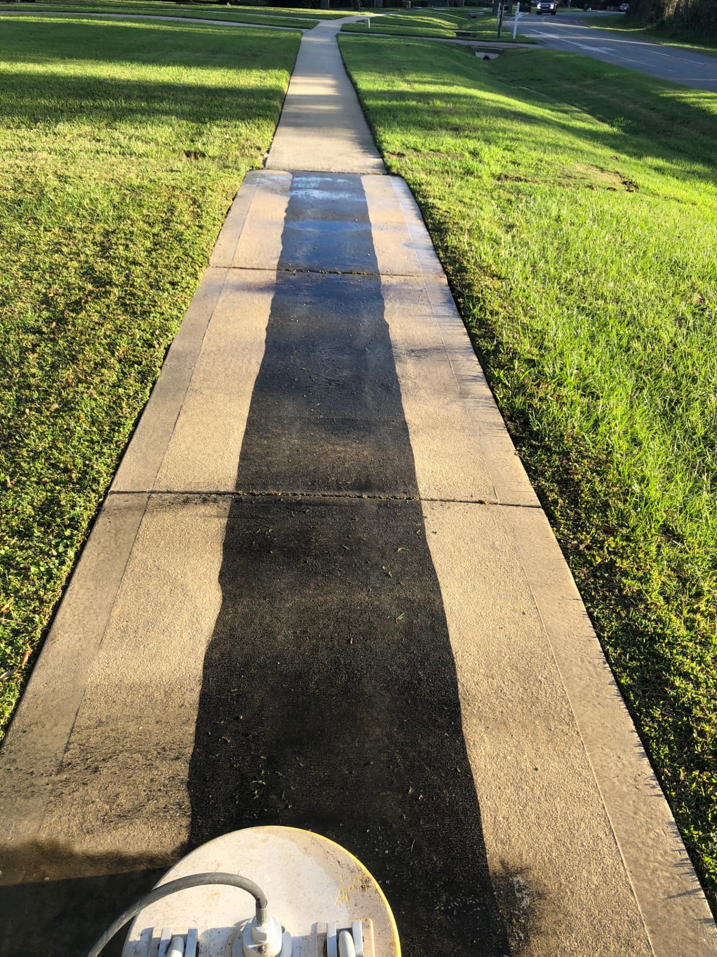 Concrete sidewalk being surface cleaned, showing a bright clean stripe next to dirty concrete